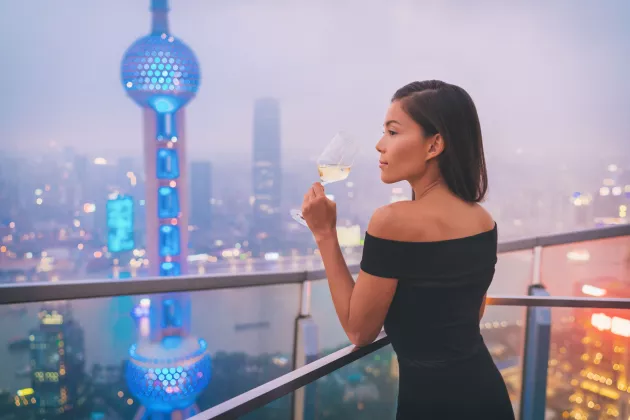 Elegante Frau in Shanghai genießt Weißwein auf einer Dachterrasse mit Blick auf die Stadt