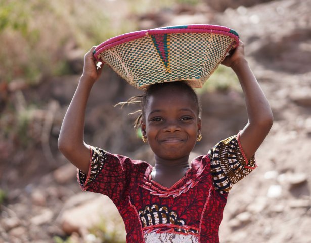 Fröhliches afrikanisches Mädchen mit Korb auf dem Kopf in der Elfenbeinküste