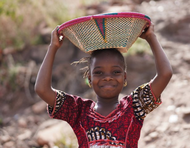 Afrikanisches Mädchen mit strahlendem Lächeln und Korb auf dem Kopf